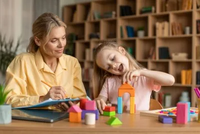 child-psychology-exam-little-girl-playing-with-colorful-wooden-blocks-professional-kids-psychologist-writing-notes